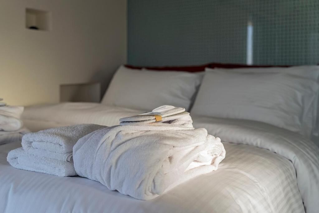 A neatly made bed with white linens and towels, a headboard, and a window with a view of the sky.