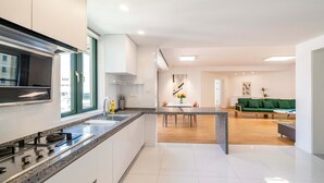 A modern kitchen with a central island, a dining area with a table and chairs, and a green sofa in a living room.