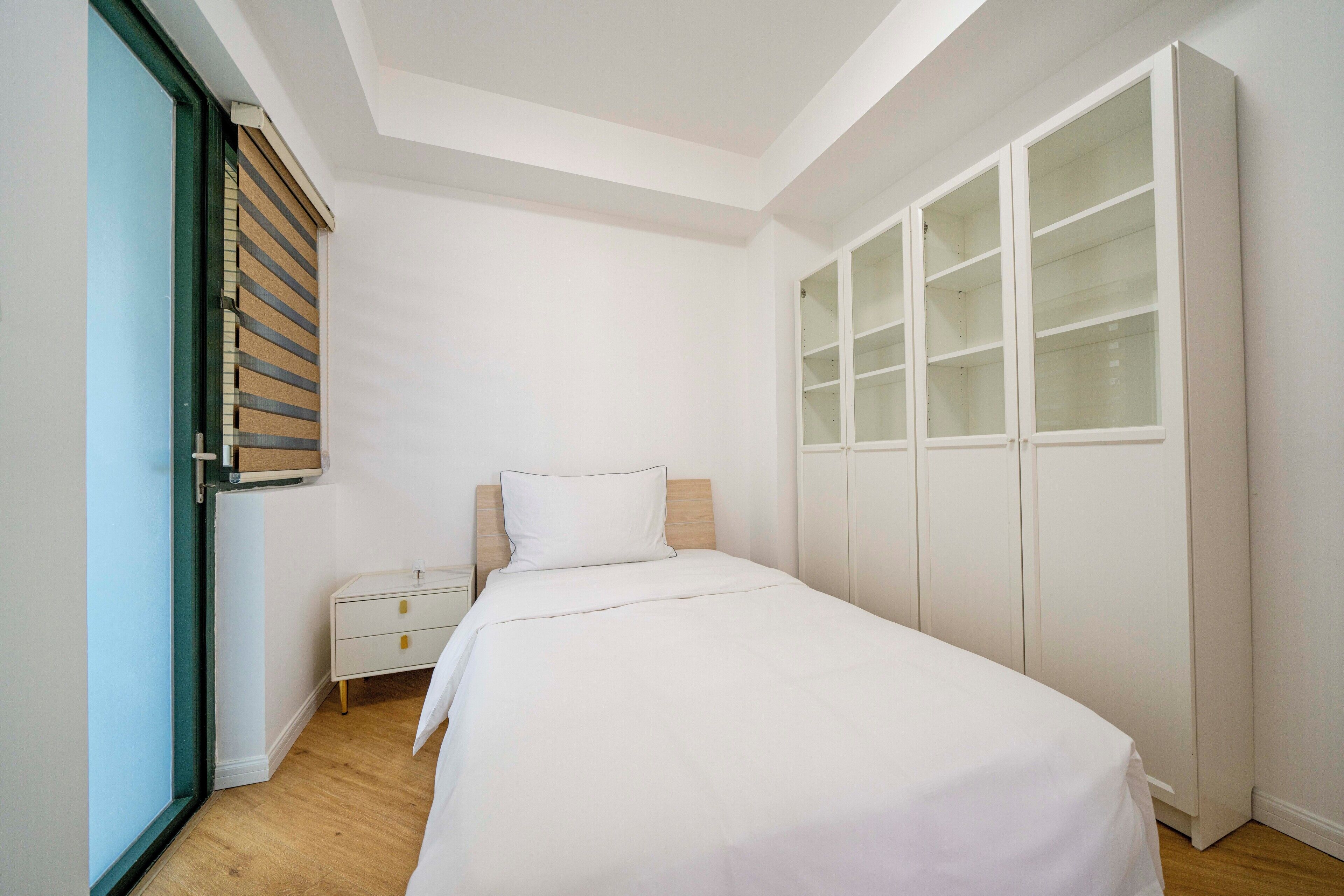 A bedroom with a bed, a nightstand, a wardrobe, and a window with blinds.