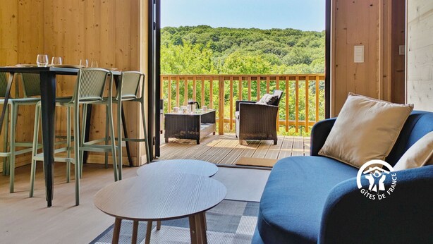 A wooden deck with a table and chairs, a sofa, and a view of a forested hill.