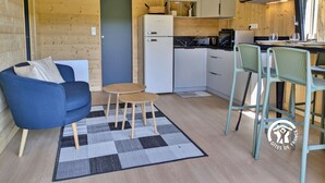 A compact kitchen with a refrigerator, microwave, and stove, a blue sofa, a small round table, and a bar area with a chair.