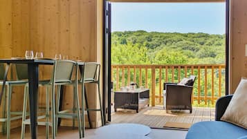 Eine Holzterrasse mit Tisch, Stühlen und einer Sitzecke, mit Blick auf einen bewaldeten Hügel.