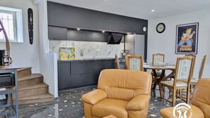 A modern kitchen with dark cabinets, a marble countertop, and a dining area with wooden chairs and a table. - Modern cottage in Louverné, sleeps 6-8, pets allowed, parking (Louverné)