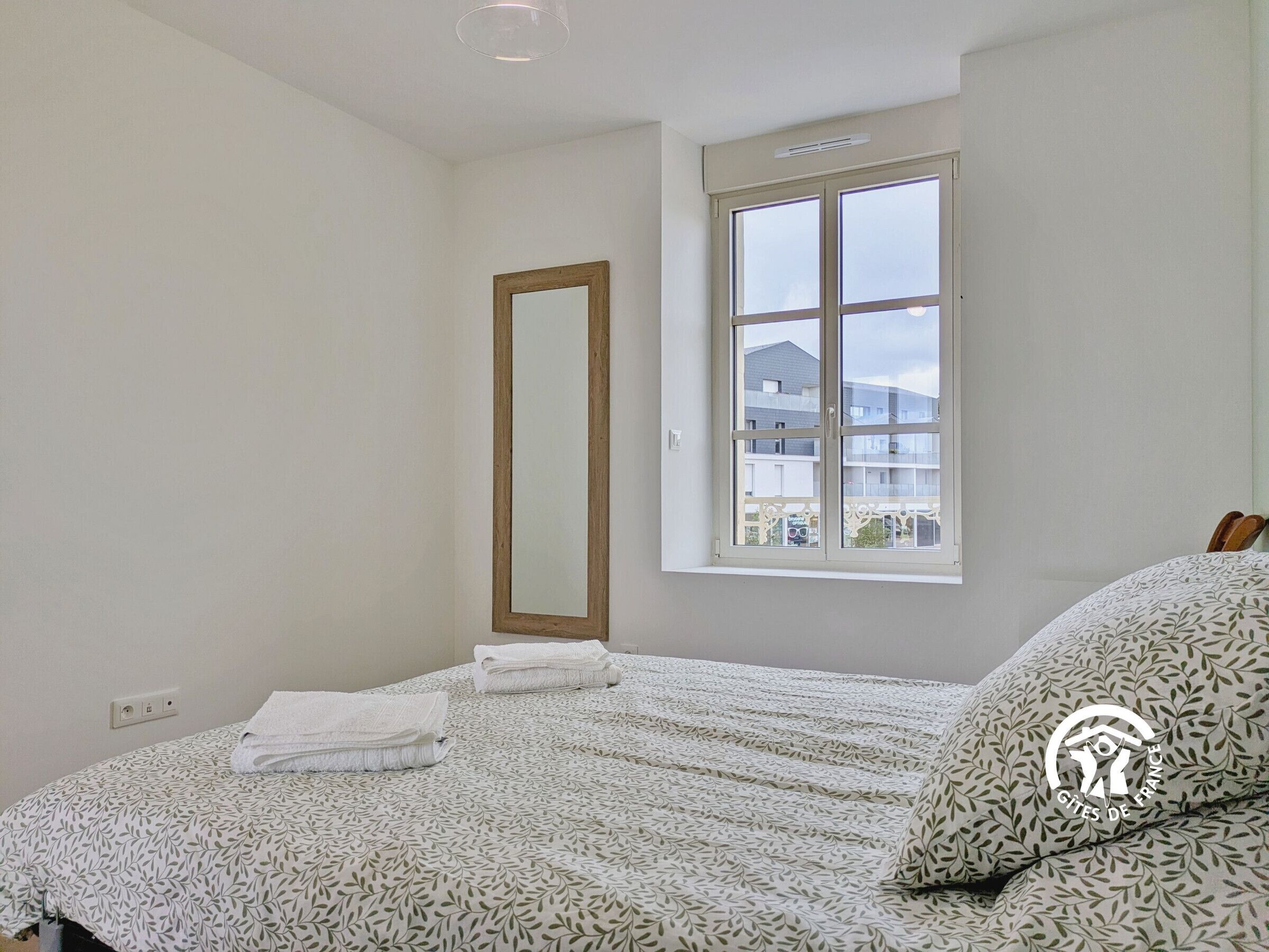 Un dormitorio con cama, ventana y espejo.