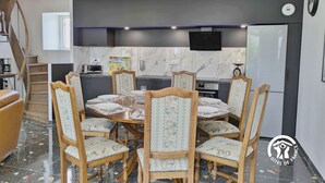 A modern kitchen with a dining area, featuring a round table with chairs, a built-in oven, and a TV mounted above the counter. - Modern cottage in Louverné, sleeps 6-8, pets allowed, parking (Louverné)