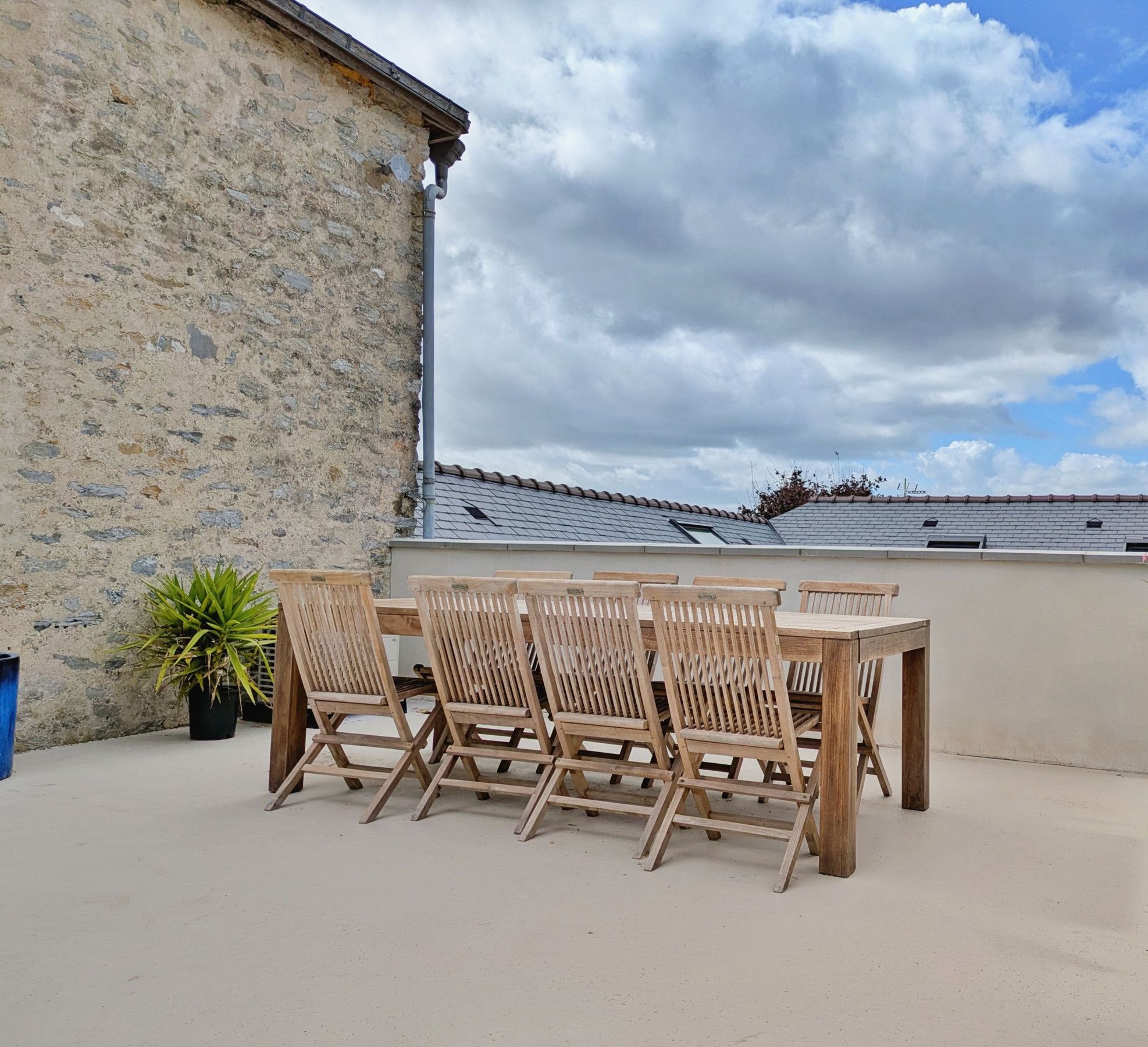 Une terrasse extérieure avec une table et des chaises en bois, un pot de fleurs et une vue sur le ciel et les nuages.