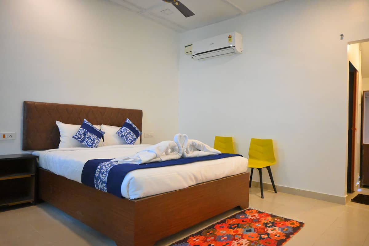 A neatly made bed with a wooden headboard, a white air conditioner on the wall, and a colorful rug on the floor.