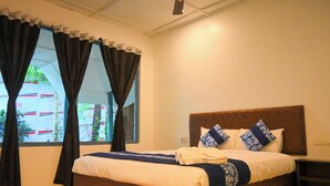 A neatly made bed with a wooden headboard, a bedside table, and a window with curtains. - Crystal Andaman Resort (Port Blair)