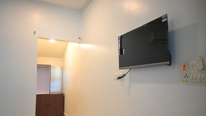A room with a flat-screen TV mounted on the wall, a wooden cabinet, and a door leading to another room. - Crystal Andaman Resort (Port Blair)