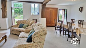 A spacious living room with a large sofa, a dining table with chairs, and a wooden cabinet. - Comfortable cottage for 6 with spacious terrace (Saint-Michel-de-la-Roë)