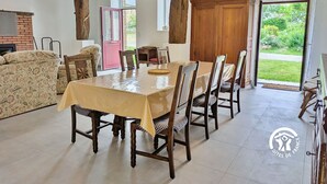 A dining area with a table set for six, wooden chairs, a sofa, and a brick fireplace. - Comfortable cottage for 6 with spacious terrace (Saint-Michel-de-la-Roë)