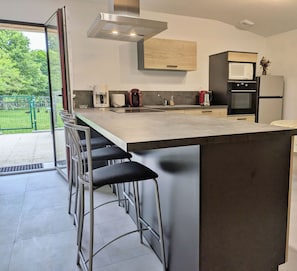A modern kitchen with a large island, bar stools, a microwave, and a refrigerator.