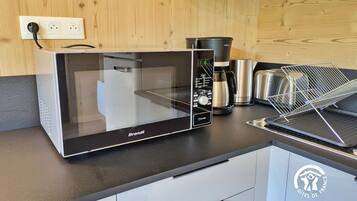 Une cuisine moderne équipée d’un four à micro-ondes de la marque Brandt, d’une machine à café et d’une étagère en métal.
