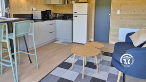 Une cuisine compacte avec des meubles blancs, un four à micro-ondes et un réfrigérateur. On y trouve un coin repas avec une table et des chaises, ainsi qu’un canapé orné d’un logo.