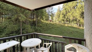 Un balcon avec une table ronde et quatre chaises, donnant sur une zone boisée.