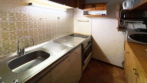 Une cuisine de taille réduite, dotée d’un évier en acier inoxydable, de meubles en bois et de carreaux décoratifs sur le mur derrière l’évier.