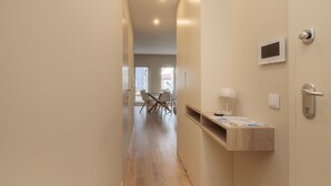 A hallway with a wooden floor, a built-in shelf with papers, a wall-mounted TV, and a door with a handle.