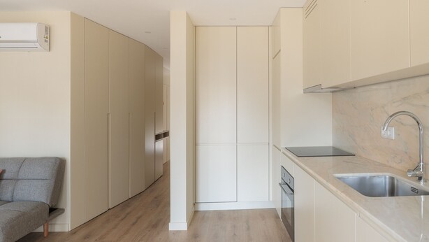 A modern kitchen with a built-in dishwasher, a marble countertop, and a grey sofa in the adjacent living area.