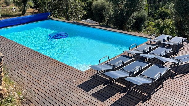 A rectangular swimming pool with a blue border, surrounded by a wooden deck with lounge chairs. - Quinta do Socalco (Caminha)