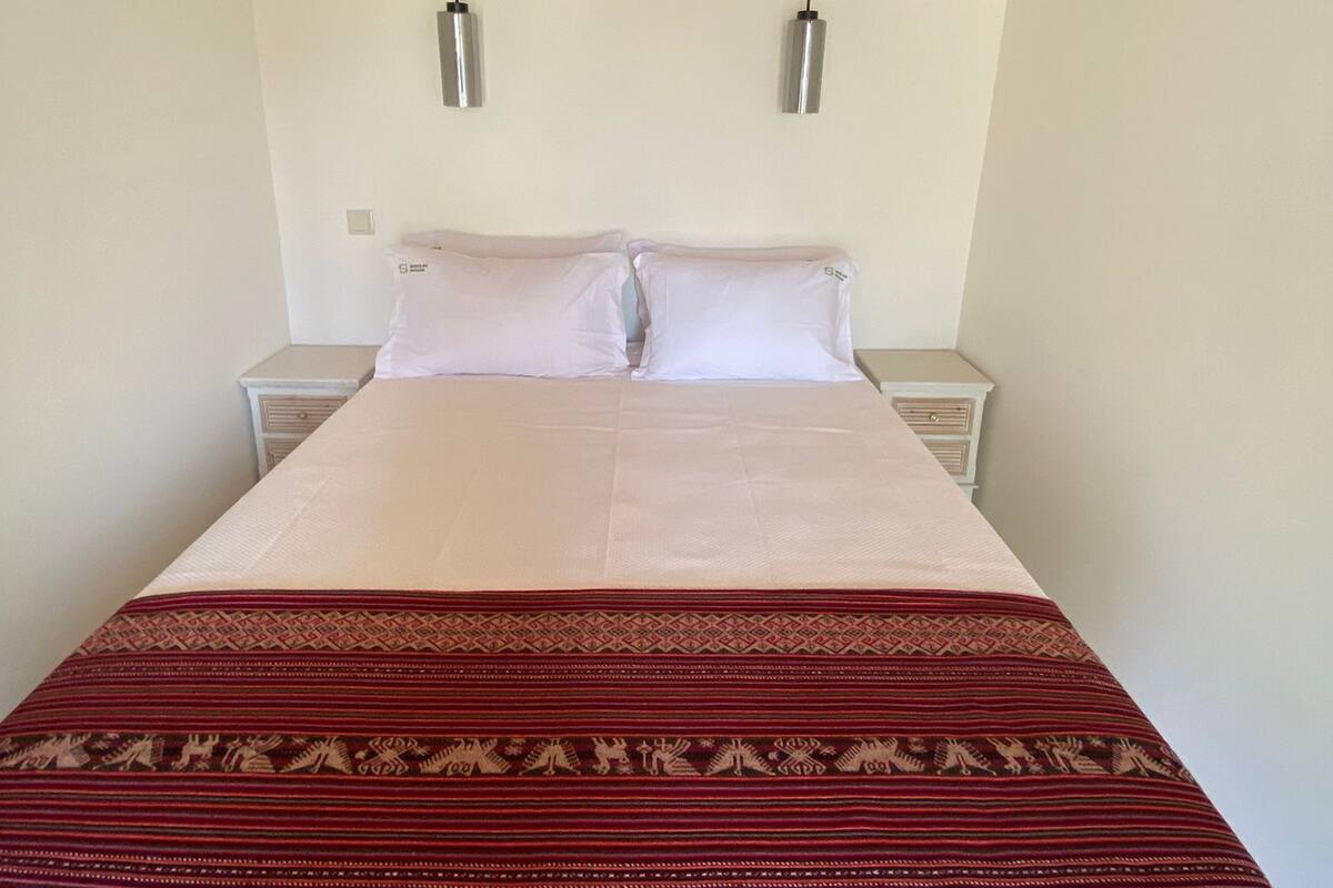 A bed with a patterned blanket, two bedside tables, and a wooden ceiling.