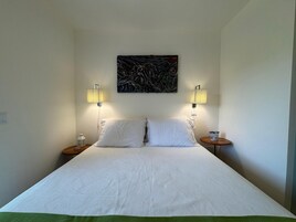 Una cama bien tendida con sábanas blancas, dos lámparas de noche y un cuadro abstracto moderno sobre la cama.