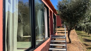 A building with large windows and a red exterior, a staircase leading to a door, and an olive tree in the background. - Quinta do Socalco (Caminha)