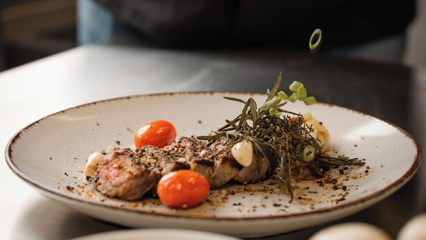 A chef seasoning a dish with herbs and tomatoes on a plate. - Saaletalstuben Hotel & Gastronomie (Graefendorf)