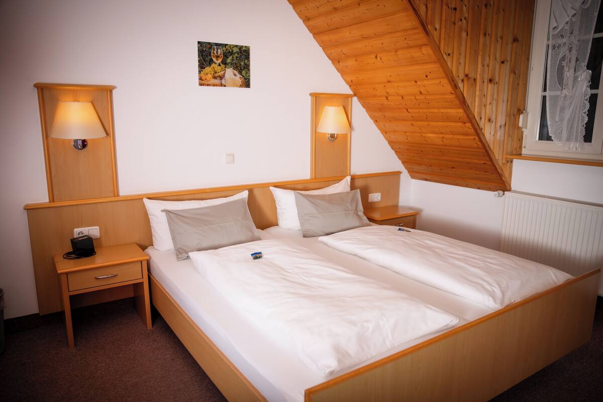 A double bed with wooden headboard and footboard, two bedside tables with lamps, a small drawer, and a picture on the wall.