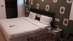 Een net opgemaakt bed met witte lakens, een nachtkastje met een lamp en een boek, en een behang met patroon achter het bed.