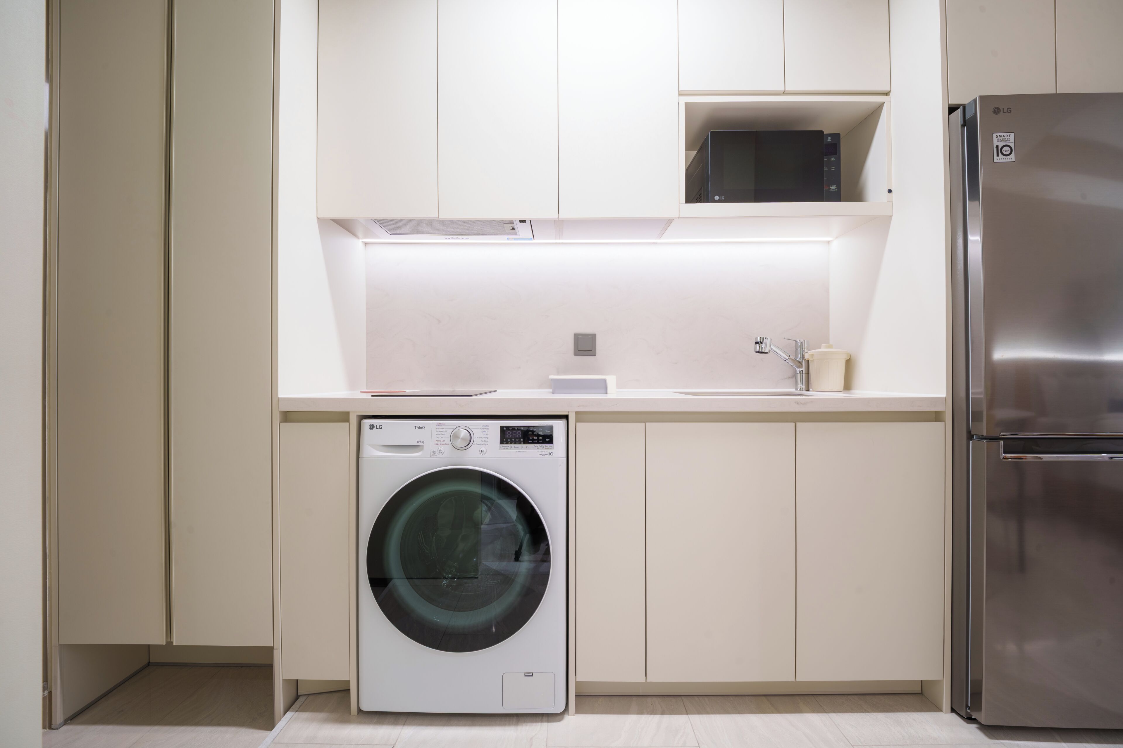 Une cuisine moderne équipée d’un réfrigérateur en acier inoxydable, d’un lave-linge et d’un four à micro-ondes.