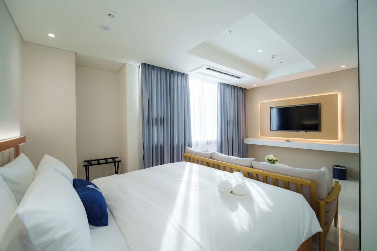 A hotel room with a bed, a TV mounted on the wall, and a window with curtains.