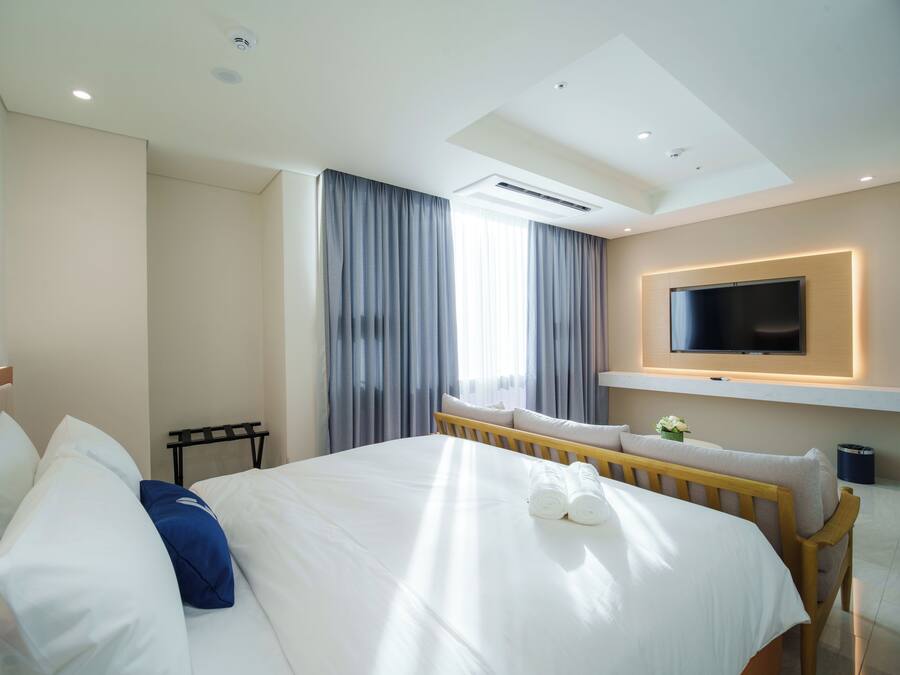 Quarto de hotel com uma cama, televisão fixada na parede e janela com cortinas.