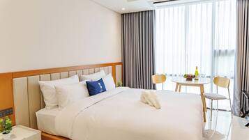 Een hotelkamer met een opgemaakt bed, een tafeltje met een fles en fruit, en een stoel.