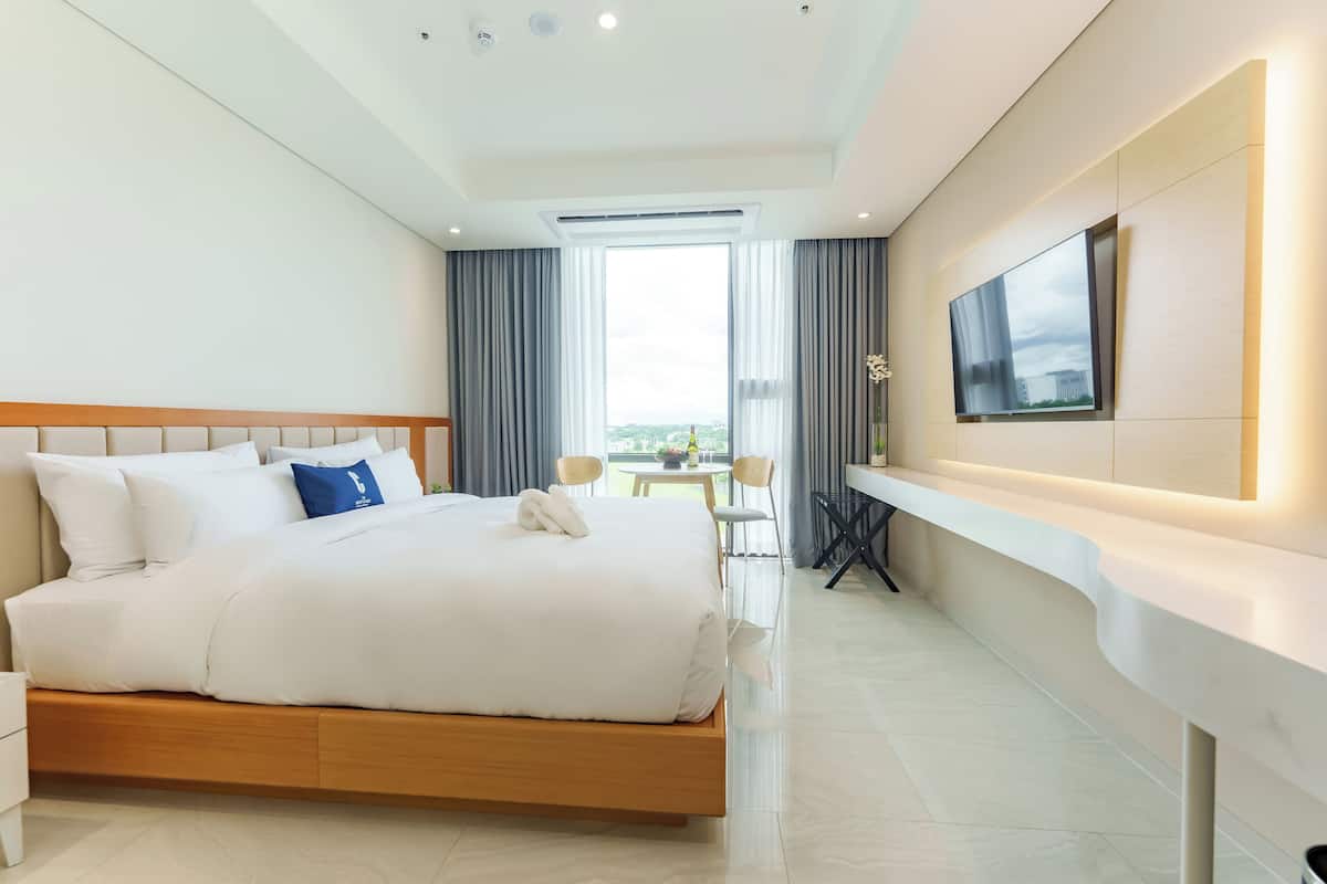 A modern hotel room with a large bed, a TV mounted on the wall, and a balcony with a view.