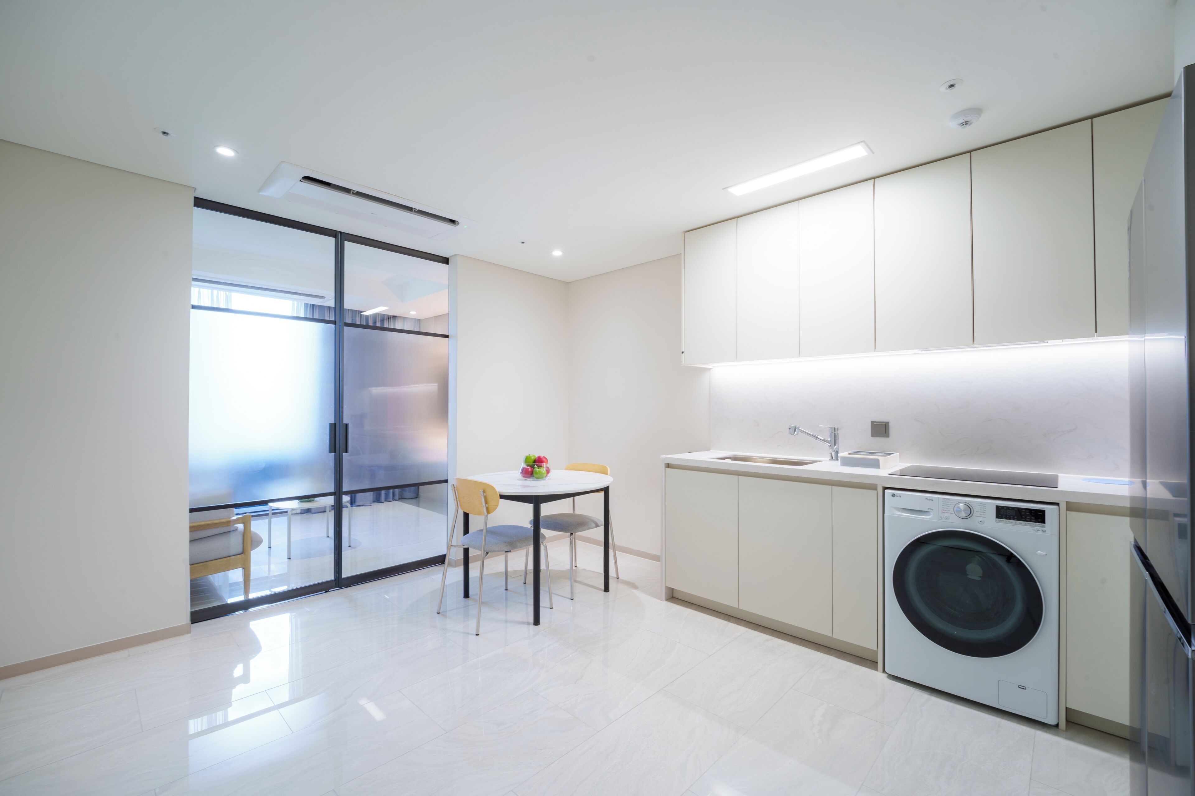 Una cocina moderna con lavadora, una mesa de comedor con sillas y un separador de vidrio.