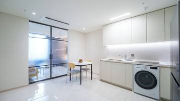 Una cocina moderna con lavadora, una mesa de comedor con sillas y un separador de vidrio.