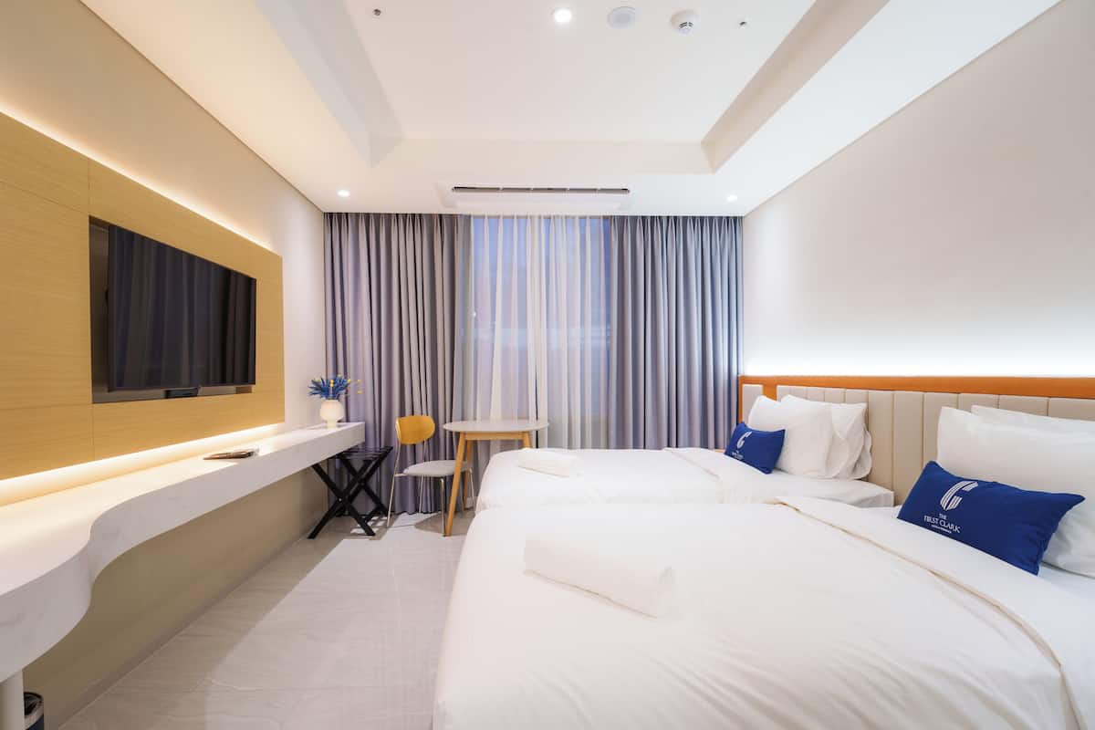 A hotel room with a bed, a desk, a chair, a TV, and a window with curtains.