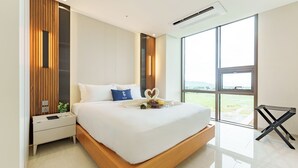 A modern bedroom with a large bed, wooden paneling, a nightstand, a bedside table, and a view of the outdoors through large windows.