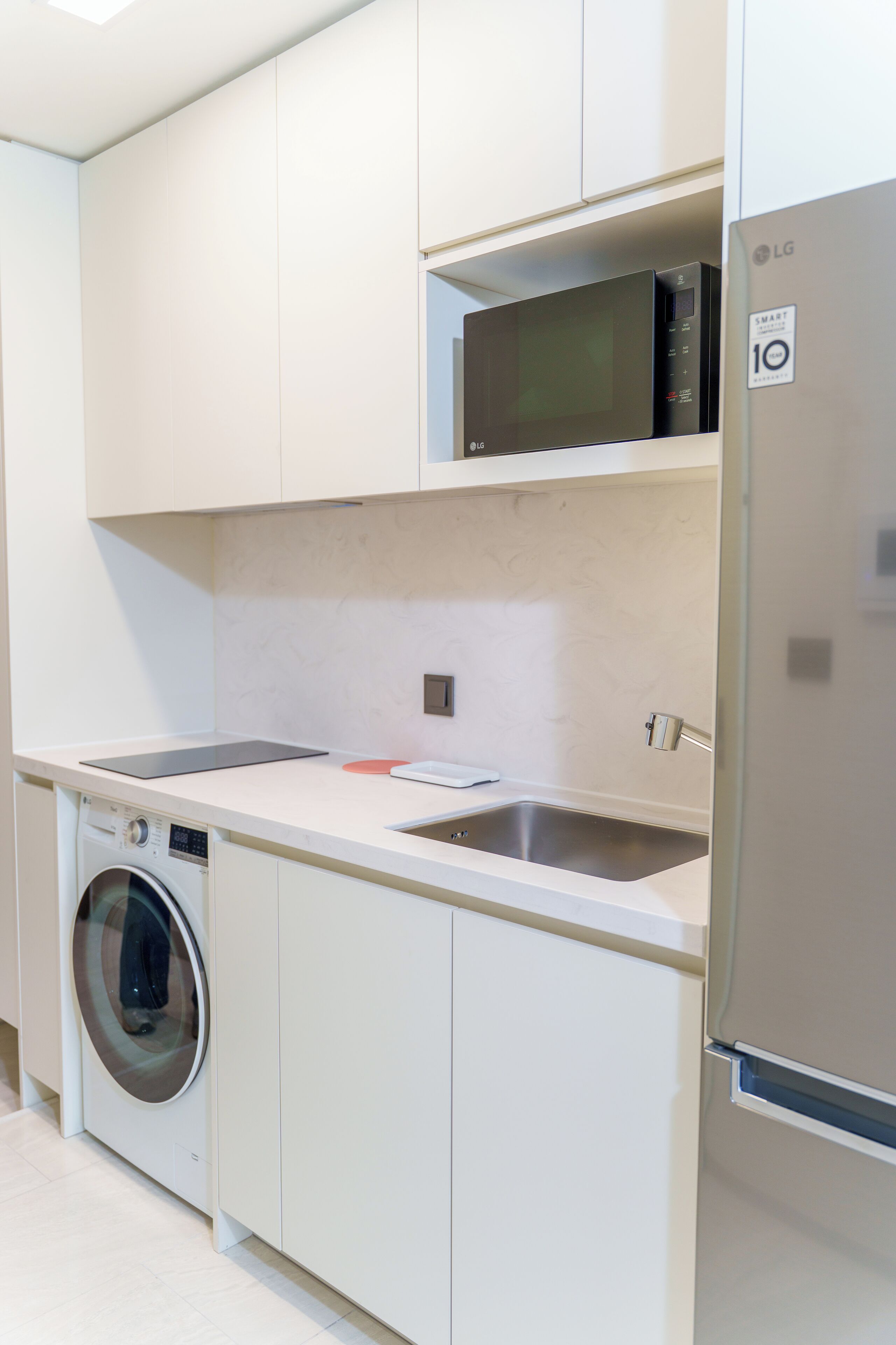 A modern kitchen with white cabinetry, a stainless steel refrigerator, a built-in washing machine, and a microwave.