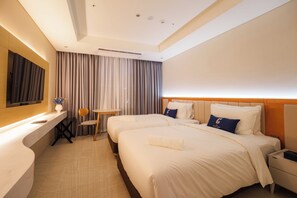 A hotel room with two beds, a desk, a chair, a TV, and a large mirror. - The First Clark Hotel & Residence (Mabalacat City)