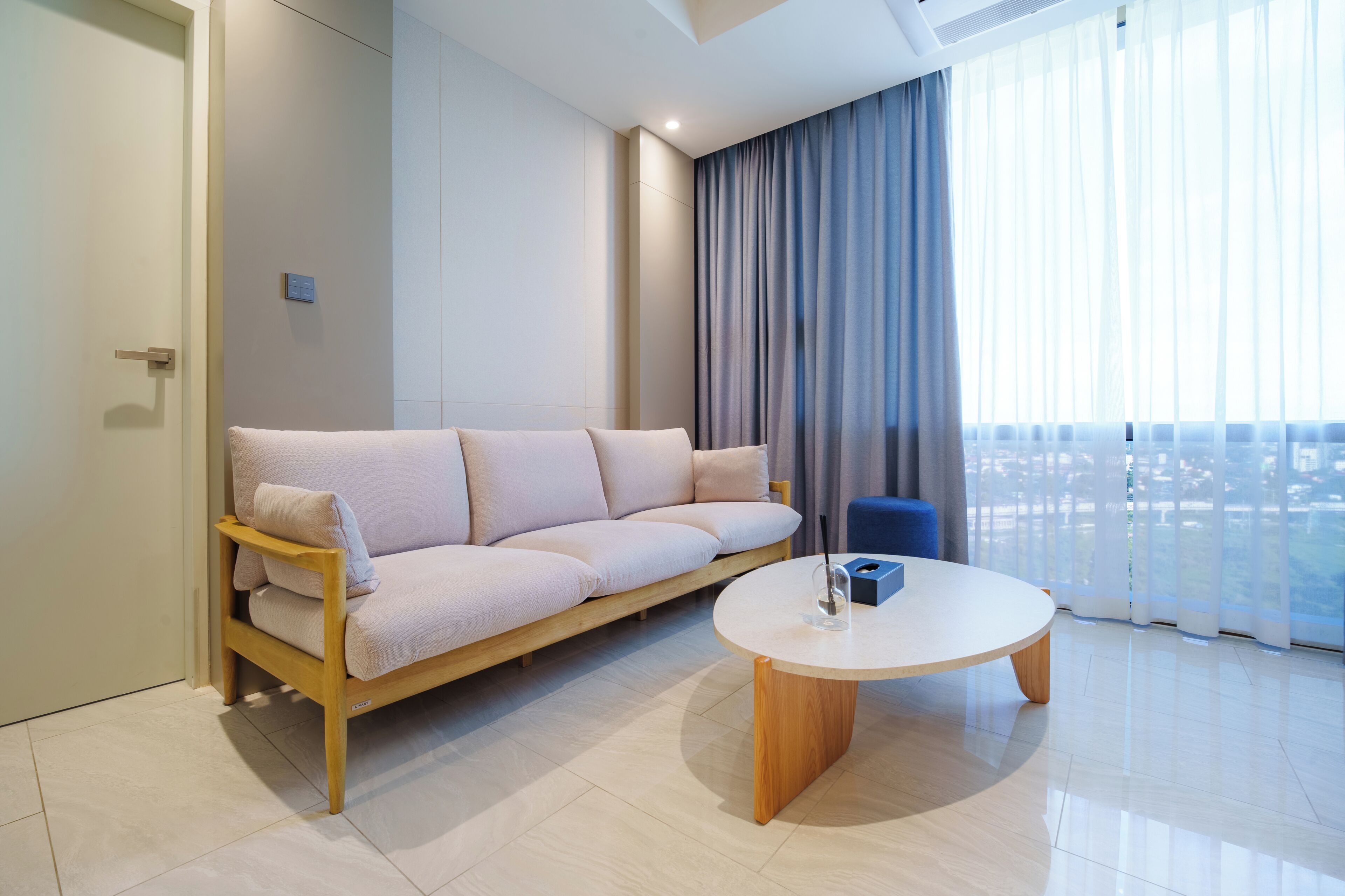 Una sala de estar moderna con un sofá, una mesa de centro y vistas de la ciudad a través de amplios ventanales.