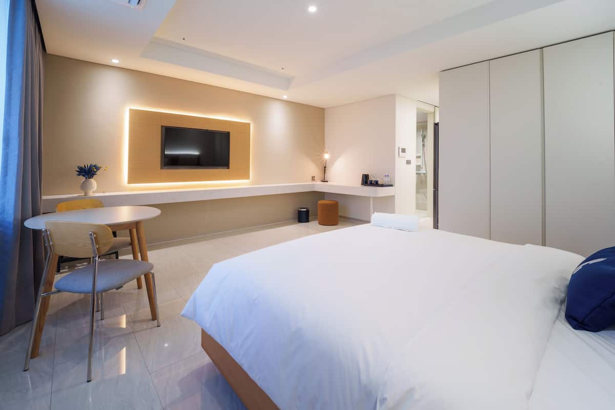 A modern hotel room with a large bed, a TV mounted on the wall, a small table, and a chair.