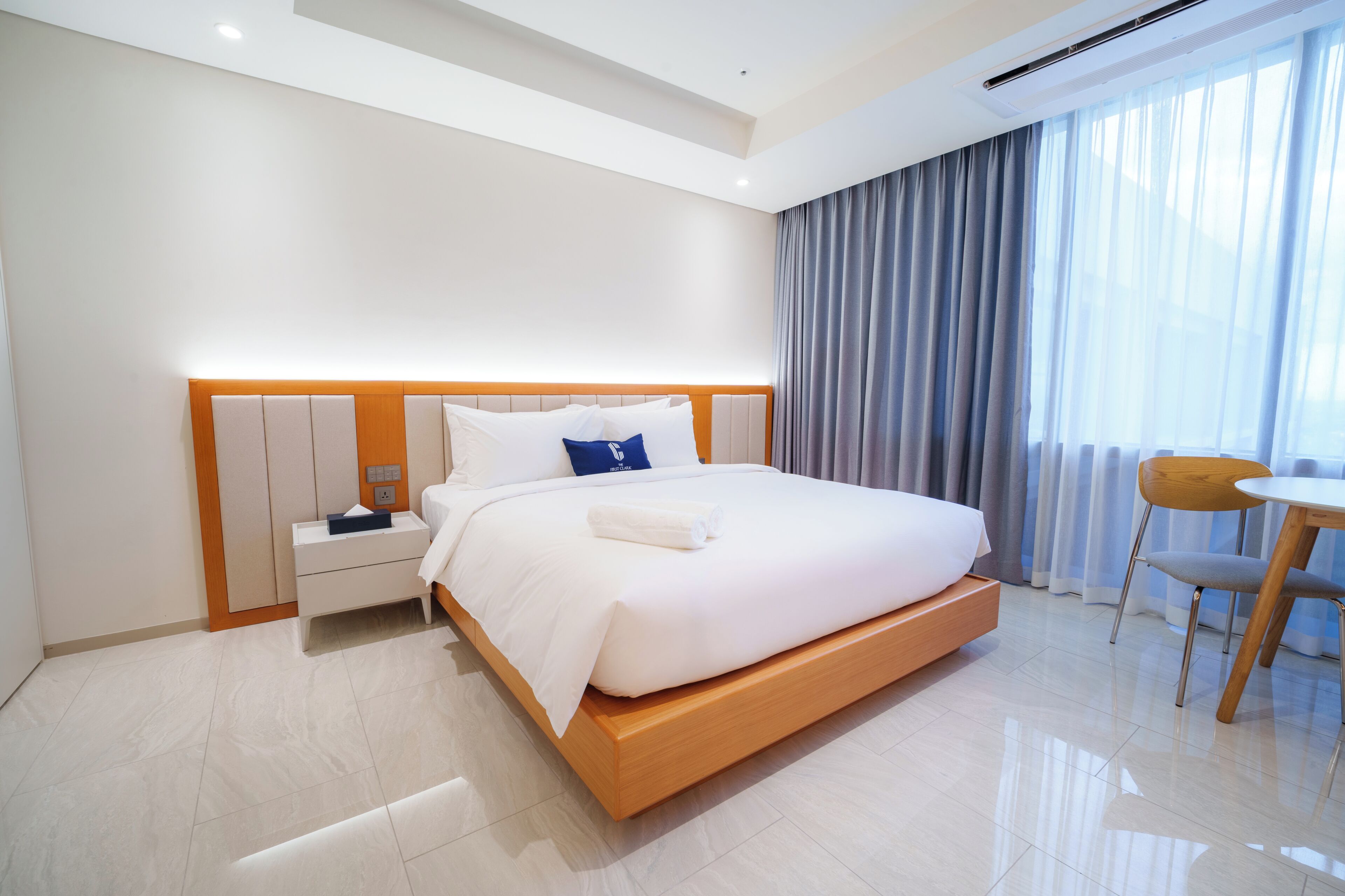 A modern hotel room with a large bed, bedside tables, a small desk, and a chair.