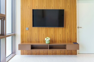 A modern living room with a wooden wall, a mounted TV, a small shelf with a vase, and a door.