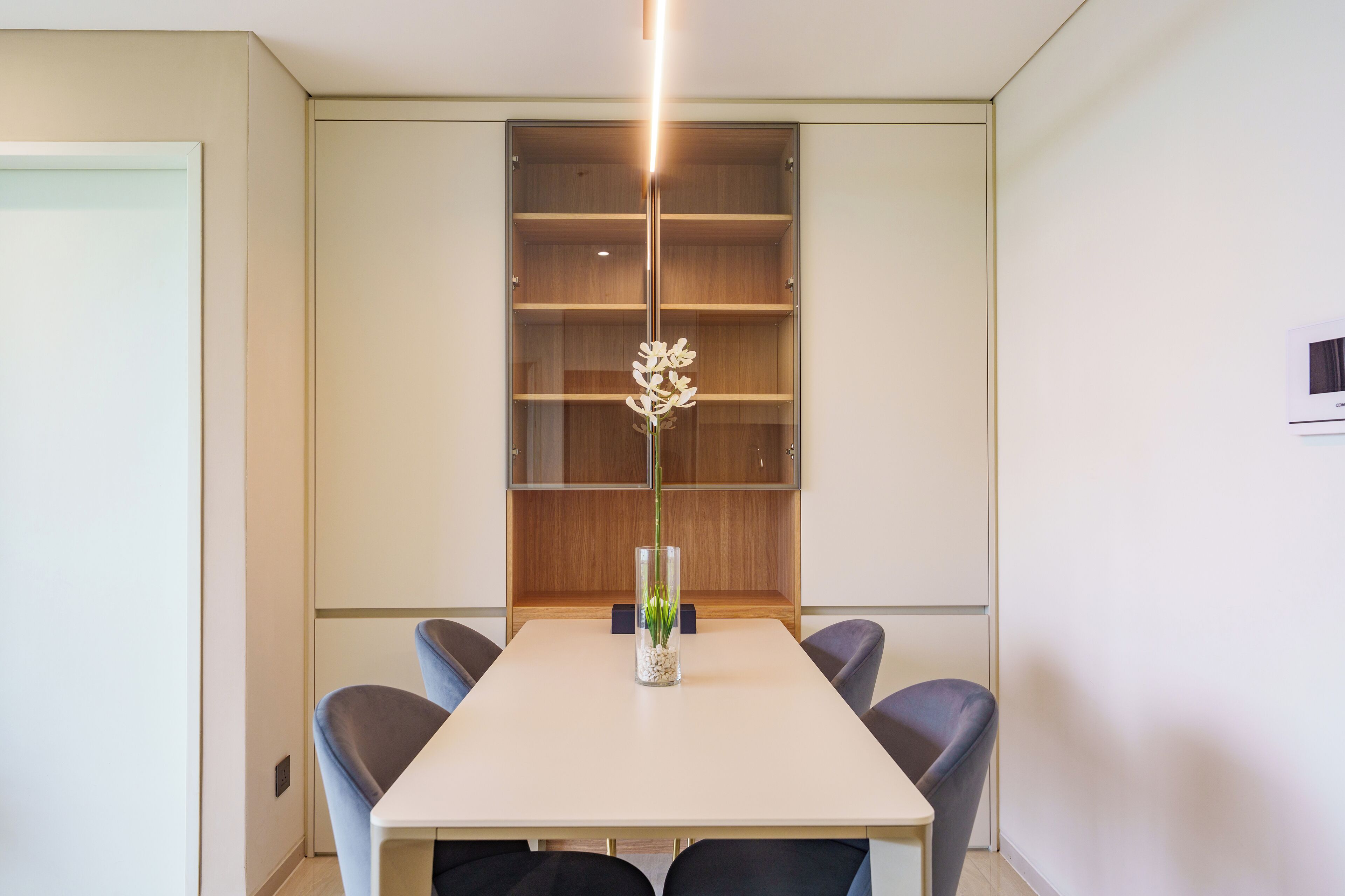 Un comedor moderno con una mesa blanca, cuatro sillas y un jarrón decorativo con flores.