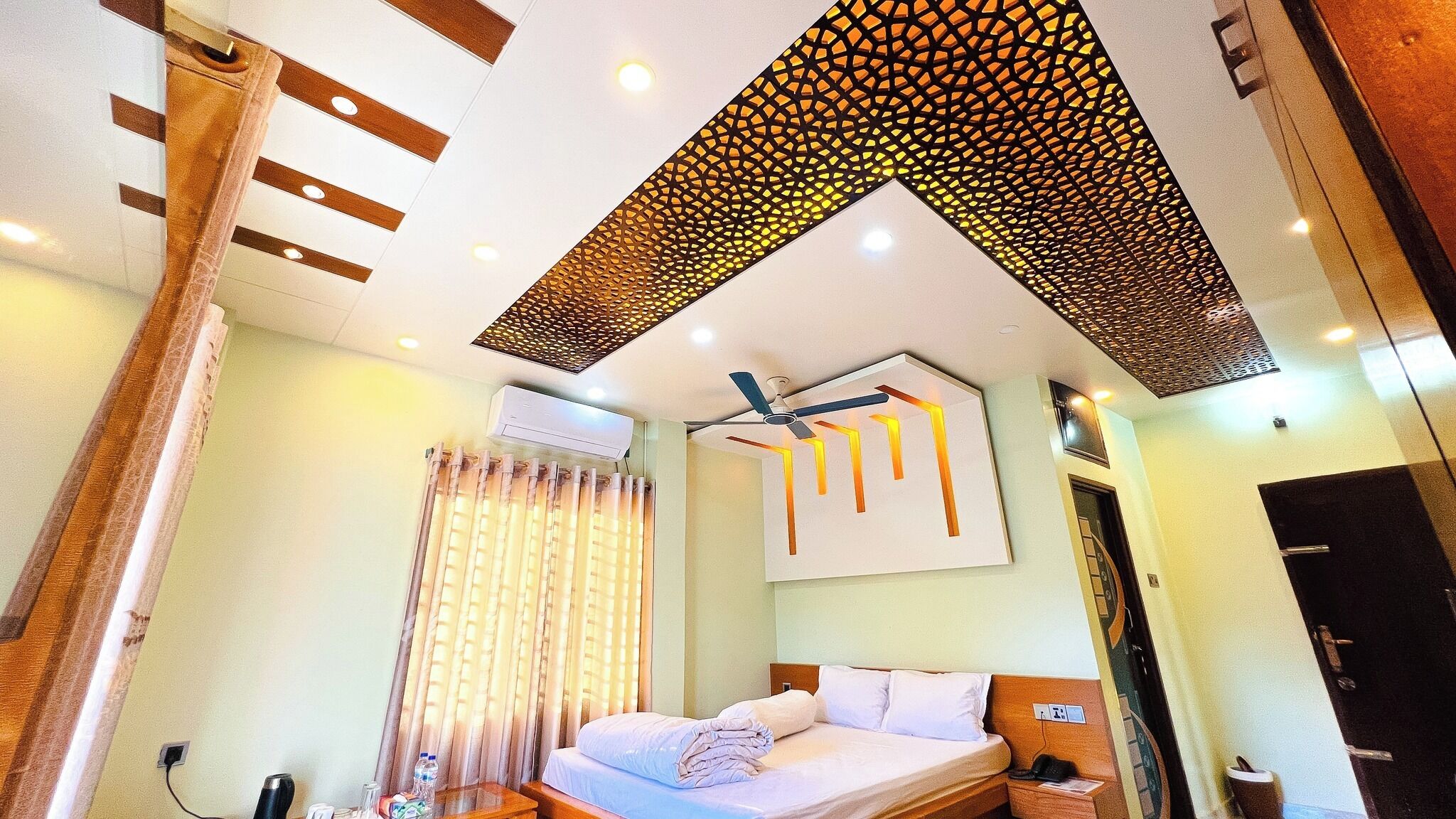 Une chambre d’hôtel équipée d’un lit, d’un ventilateur de plafond, d’un appareil de climatisation et d’une fenêtre avec des rideaux.