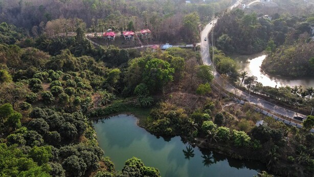 An aerial view of a lush area with a small pond, a bridge, and a road. - Mountain Springs Resort (Bandarban)