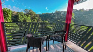 Een balkon met twee stoelen en een tafel, met uitzicht op een weelderig groen bos.