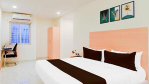 Habitación de hotel con una cama grande, un escritorio y una silla. Se ve una ventana con persianas, un aire acondicionado instalado en la pared y tres cuadros enmarcados.