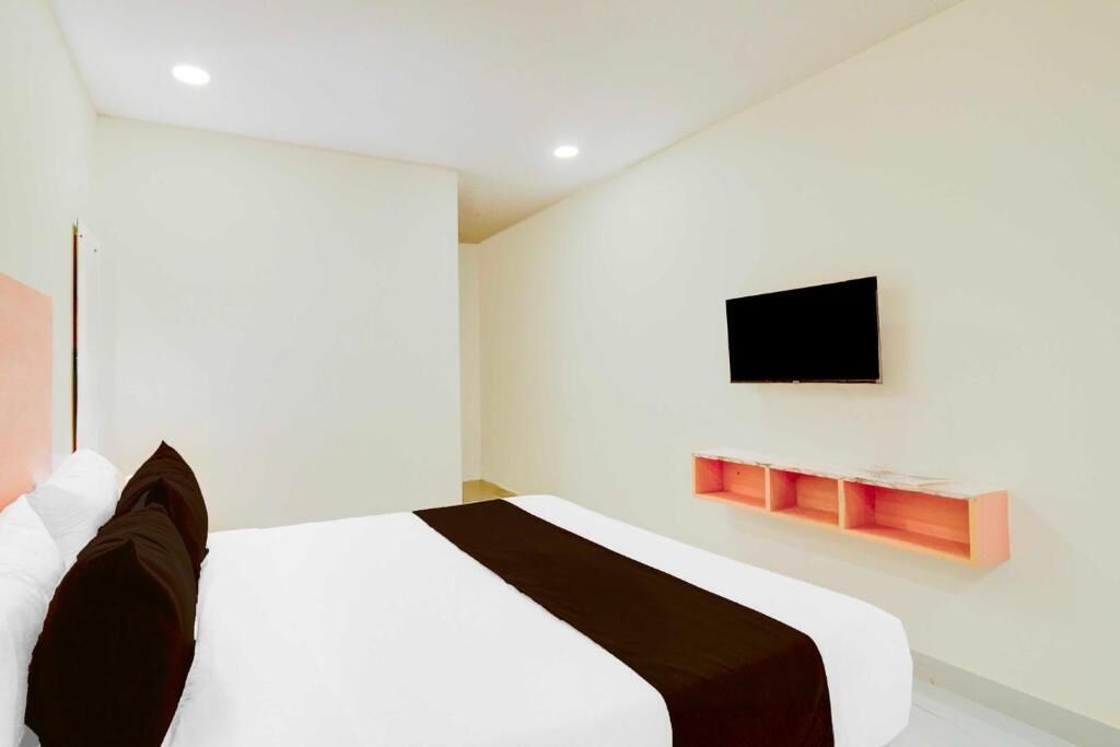 Una habitación de hotel moderna con una cama grande, televisor montado y estanterías integradas.